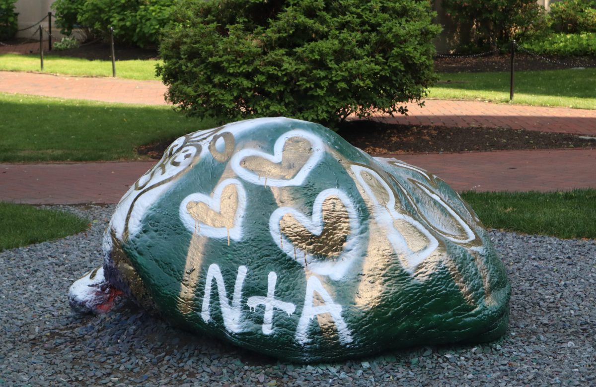 Greek Rock decorated in green and gold behind the School of Law. BU students participate in a variety of traditions, including hockey games, club rock paintings, and even late night slices at T. Anthony's Pizzeria. 